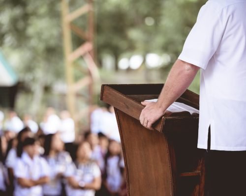 A closeup shot of a male standing near a wooden stand reading the bible for children